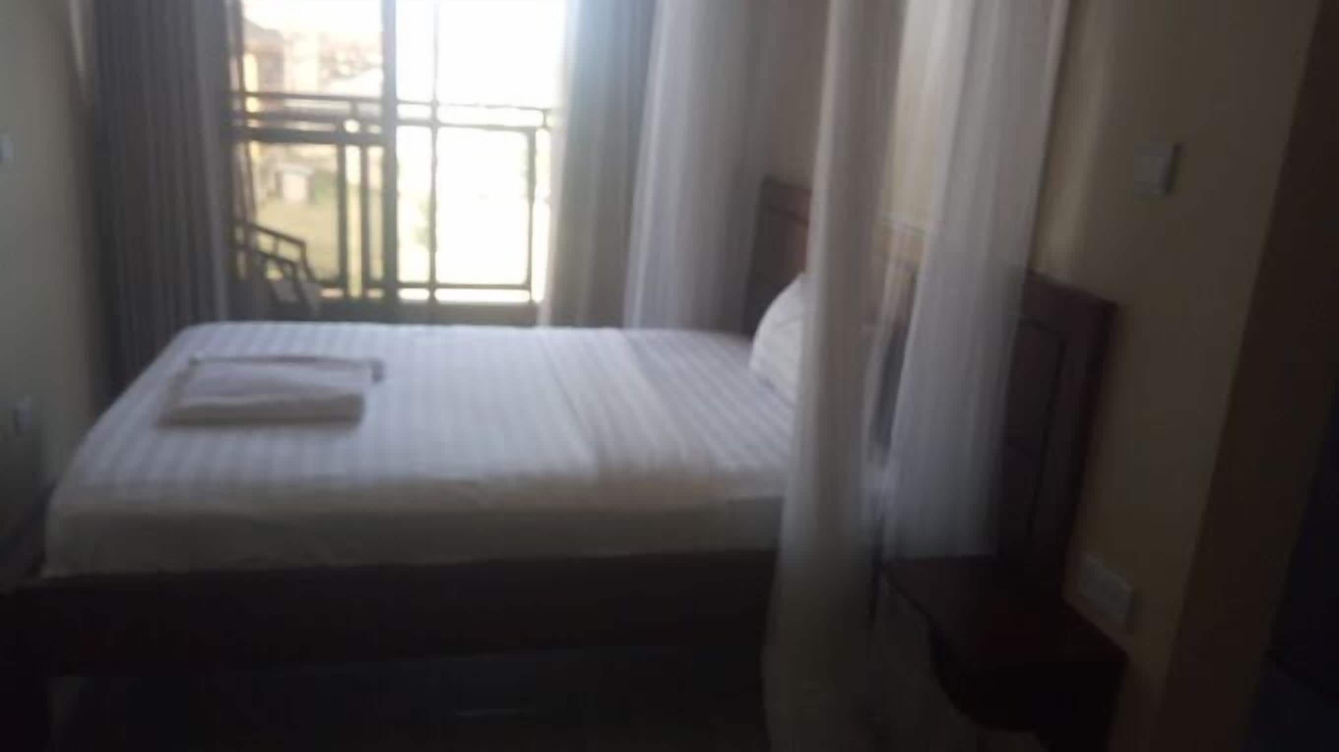 A hotel room with a bed, a window with curtains, and a view of the outside.