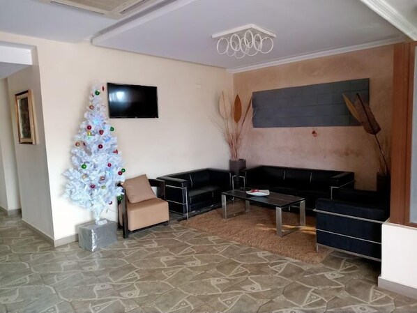 A living room with a white Christmas tree, a black leather sofa, a coffee table, and a flat-screen TV mounted on the wall. - Rockwell Hotel (Kisumu)