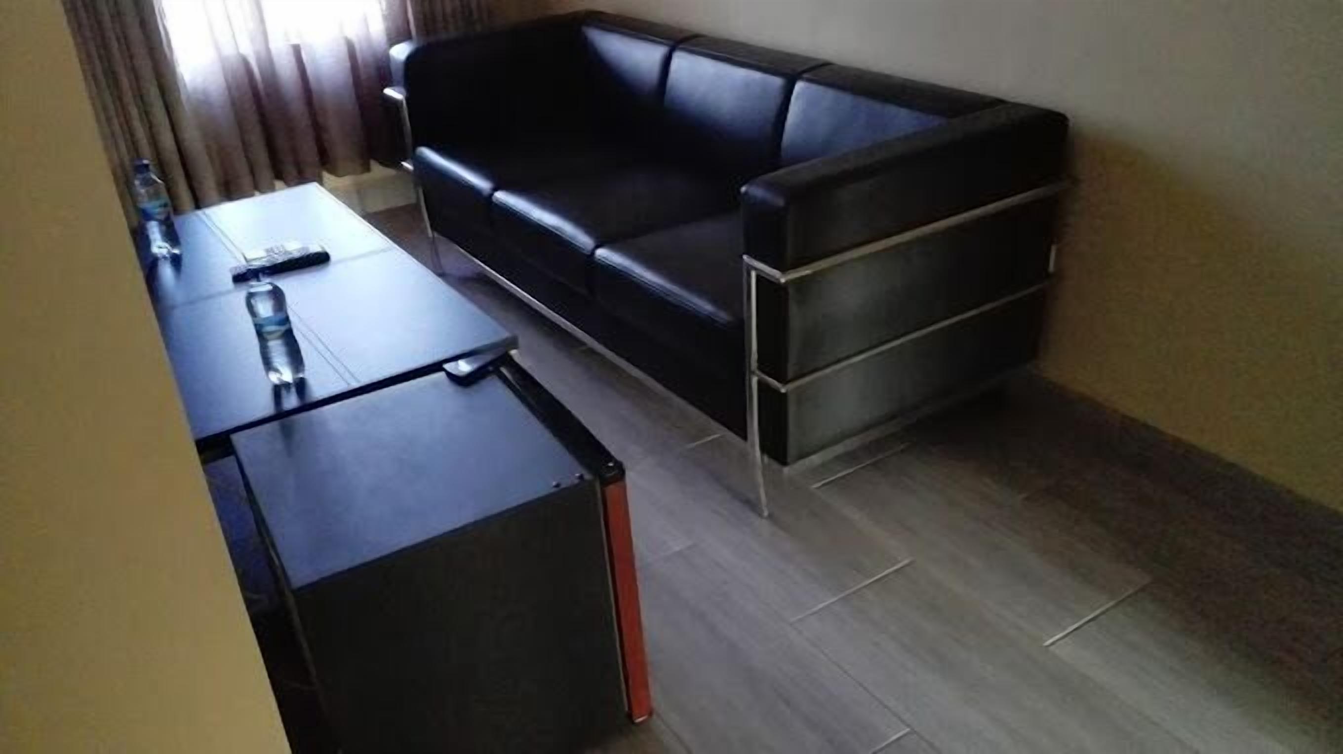 Un petit espace de vie moderne comprenant un canapé en cuir noir, une petite table et une kitchenette compacte.