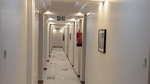 A long, well-lit hallway with a fire exit sign, tiled floors, and framed pictures on the walls. - Rockwell Hotel (Kisumu)