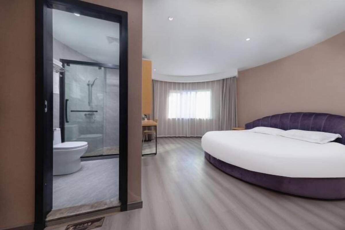 Una habitación de hotel moderna con una cama grande, un box de ducha con paredes de vidrio y un inodoro separado.