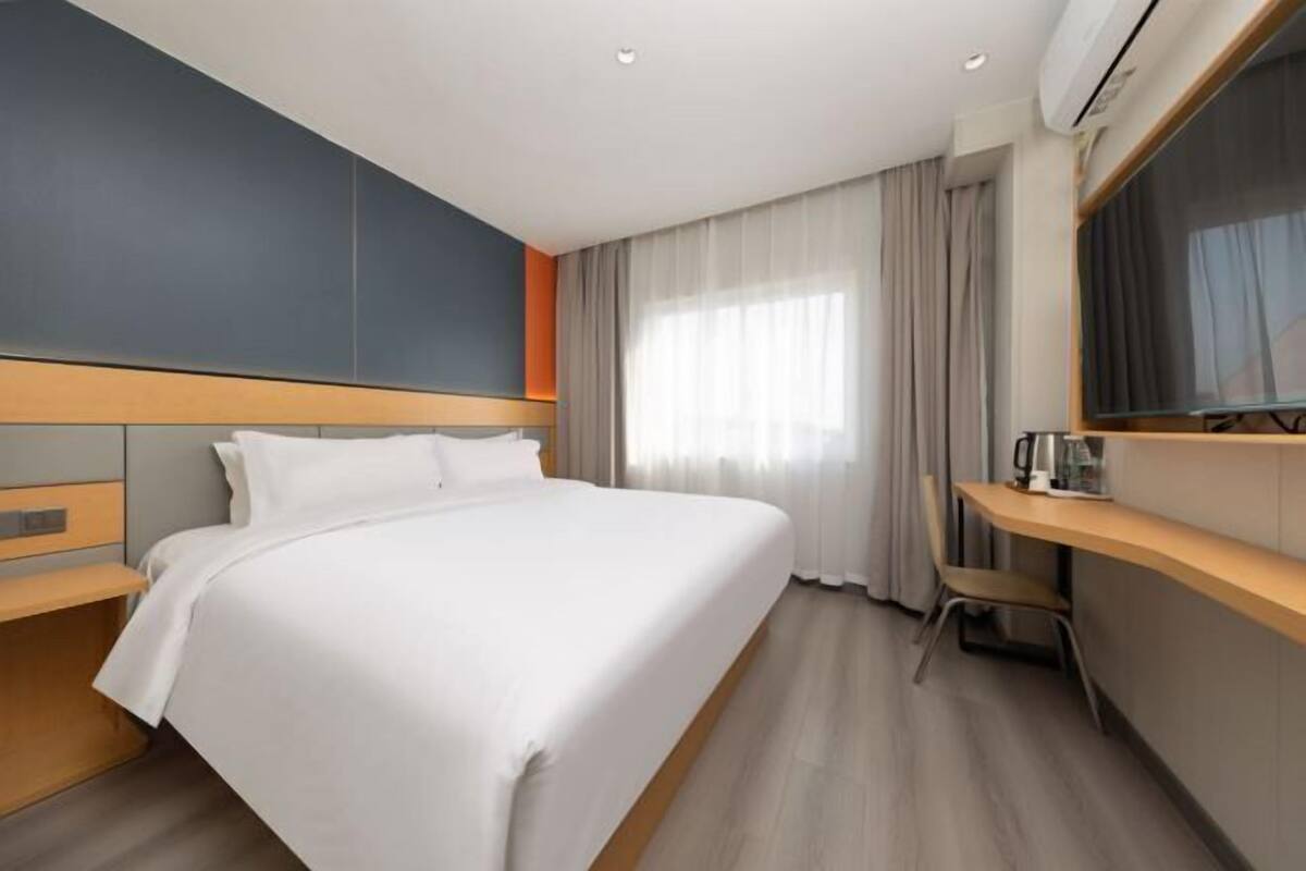 Habitación de hotel con cama, escritorio, silla y un ventanal con cortinas.