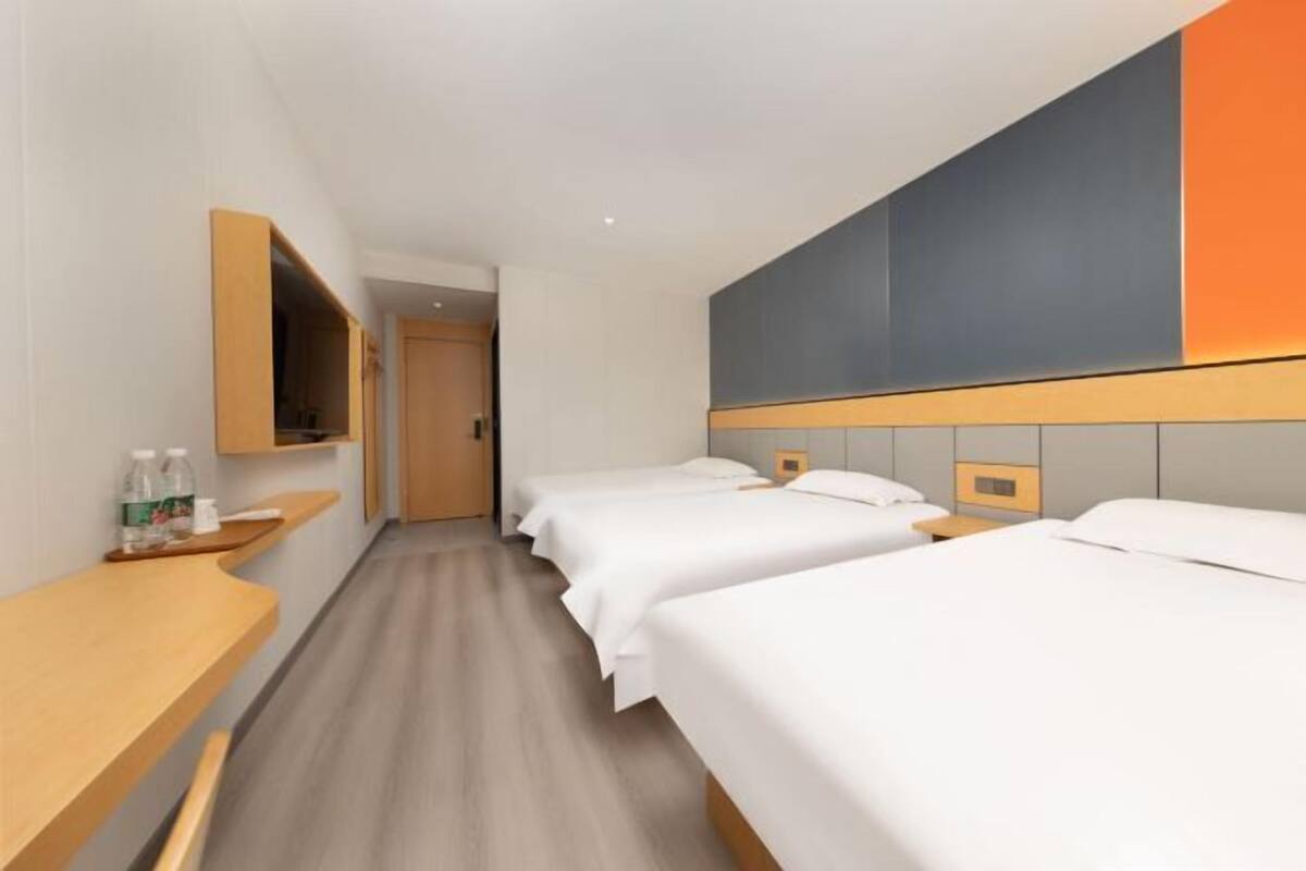 Habitación de hotel con tres camas, un escritorio de madera, un espejo y una pared con diseño geométrico.