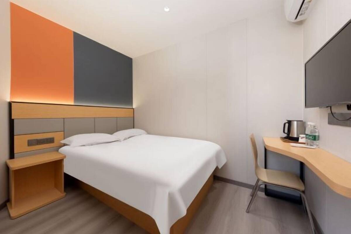 Una habitación de hotel con cama, mesita de noche, silla, escritorio y televisor de pantalla plana.