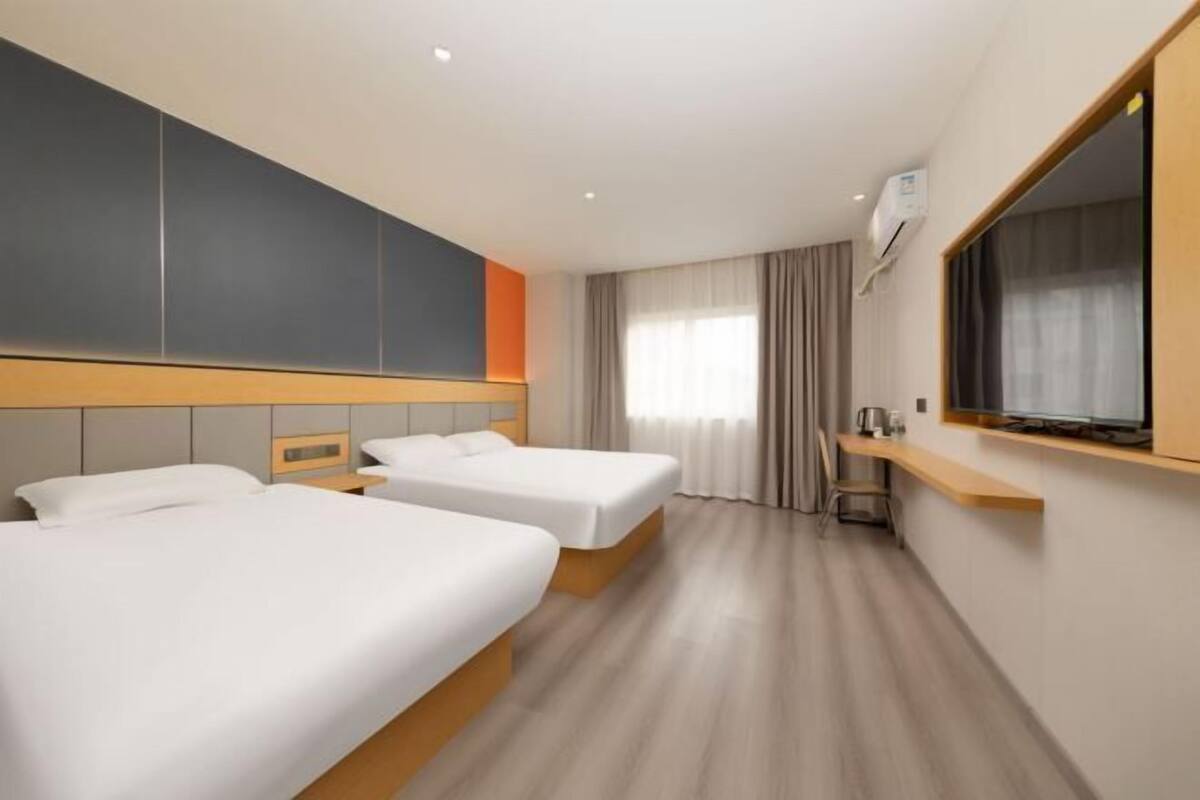 Una habitación de hotel con dos camas, televisión, ventana con cortinas y cabecera de madera.
