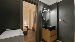A modern bathroom with a dark wall, a round mirror, a black sink, and a white washing machine.