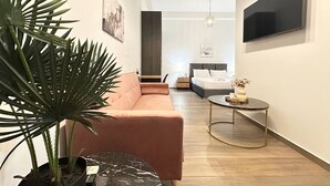 A modern living room with a sofa, a coffee table, a TV mounted on the wall, and a large plant.