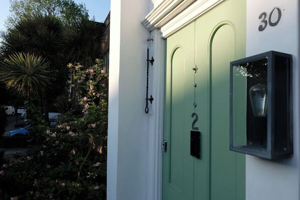 A green door with the number 30, a mailbox, and a small window on a white wall.