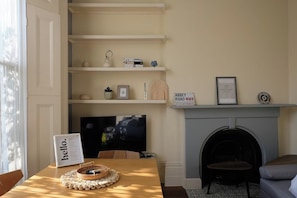 A living room with a fireplace, a television, and a table with a basket and a sign.