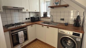 Una cocina compacta con armarios blancos, horno integrado, lavadora y cafetera.