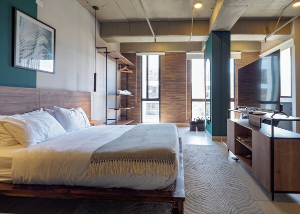 Camera d'hotel moderna con un letto grande, TV, scrivania e vista sulla città.