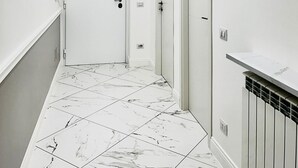 A hallway with white walls, a marble floor, and a radiator on the right.