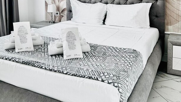 A modern bedroom with a tufted headboard, white bedding, and a large floral-patterned wall.