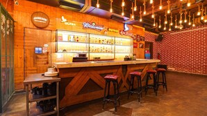 A bar area with a wooden counter, stools, and a variety of liquor bottles. - Super Townhouse Oak Silver City Chowk (Dehradun)