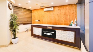 A reception desk with a wooden panel wall, a clock, and a potted plant. - Super Townhouse Oak Silver City Chowk (Dehradun)