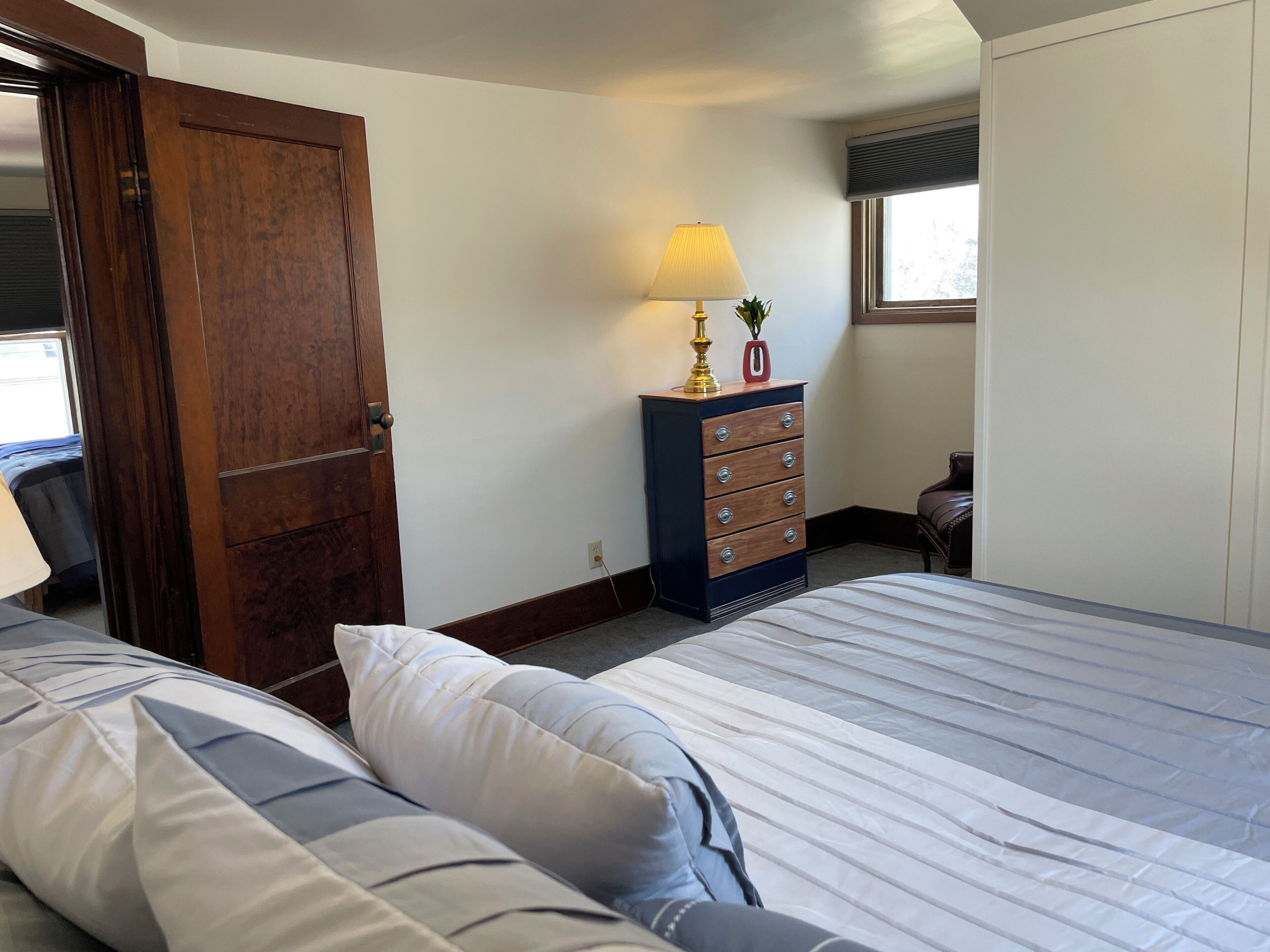 A bedroom with a bed, a dresser, a lamp, and a window.
