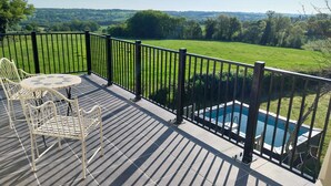 A deck with a pool, chairs, and a view of a green landscape.