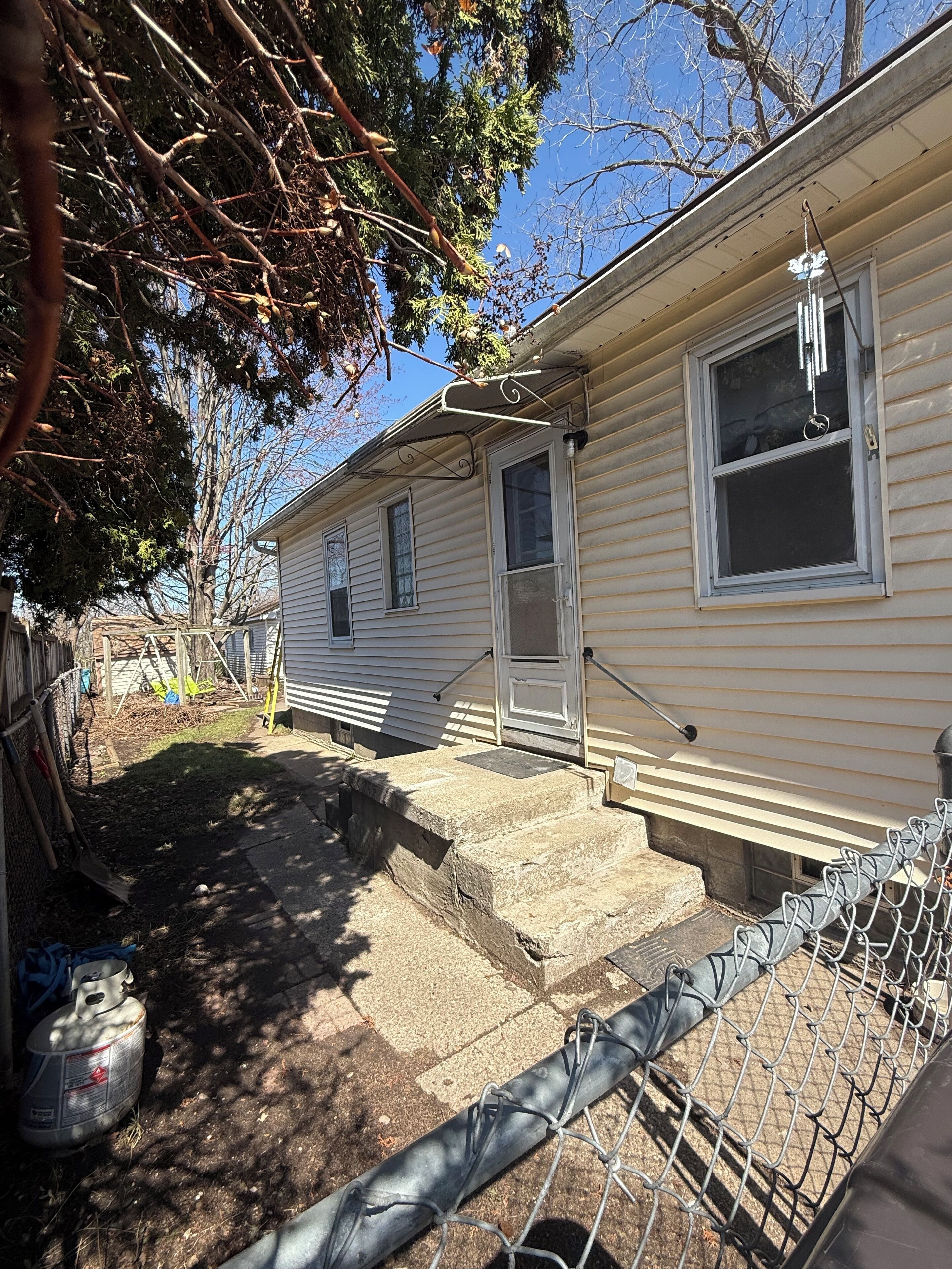 A single-story house with a front porch, a small yard, and a chain-link fence.