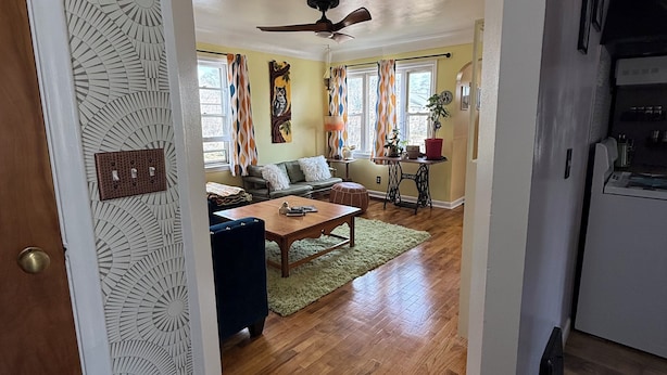 A spacious living room with a wooden floor, a ceiling fan, and a dining area with a table and chairs.
