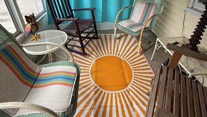 A cozy porch area with two wicker chairs, a small table, and a colorful sun-patterned rug.
