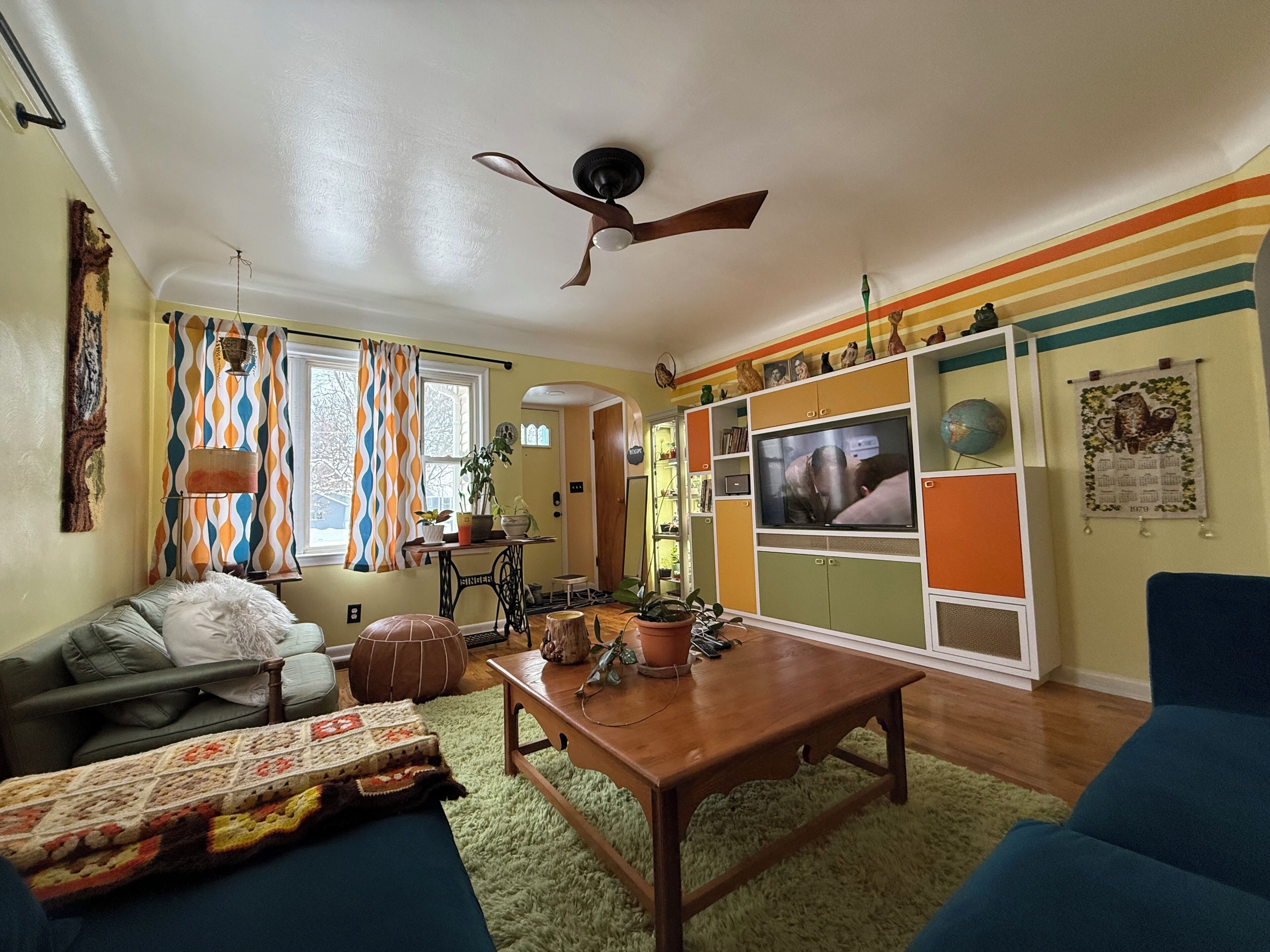A cozy living room with a wooden coffee table, a sofa, and a TV mounted on a colorful wall.