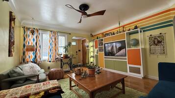 A cozy living room with a wooden coffee table, a sofa, and a TV mounted on a colorful wall.