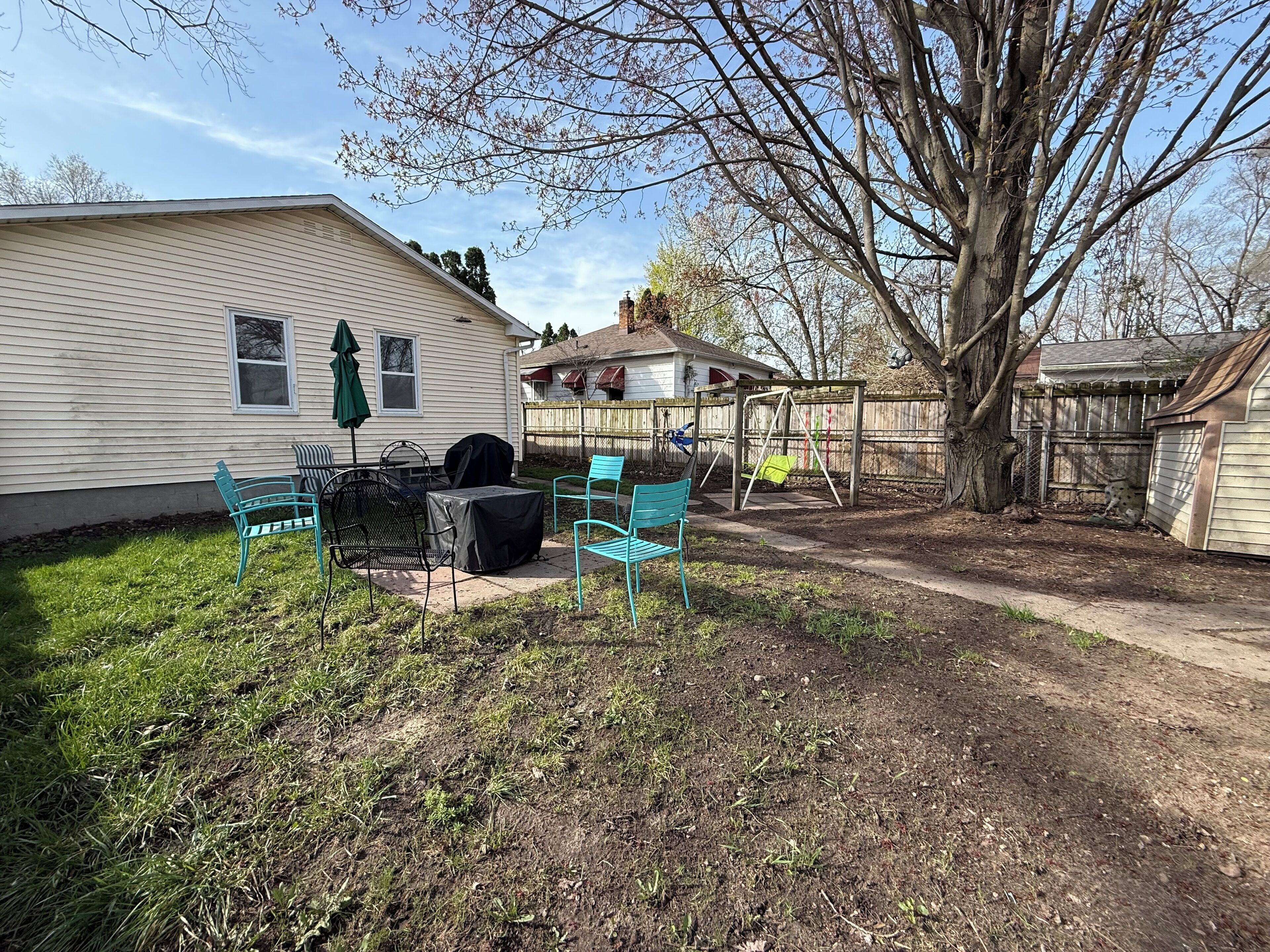 A backyard with a patio area, a swing set, and a covered barbecue grill.