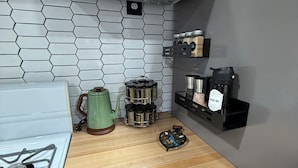 A kitchen with a white stove, a microwave, a wooden countertop, a green kettle, a spice rack, and a black coffee maker.