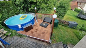 A backyard with a swimming pool, a wooden deck, a sofa, and a trampoline. - Cozy and quiet vacation apartment with private garden in beautiful Thuringia (Schmalkalden)
