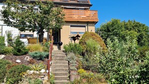 A house with a stone staircase leading to the front door, surrounded by various plants and shrubs. - Cozy and quiet vacation apartment with private garden in beautiful Thuringia (Schmalkalden)
