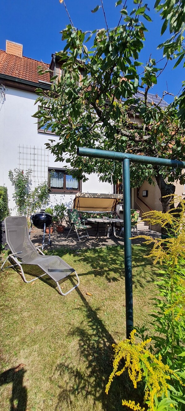 A backyard with a metal chair, a grill, and a tree. - Cozy and quiet vacation apartment with private garden in beautiful Thuringia (Schmalkalden)