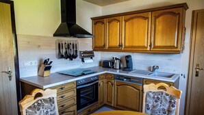 A kitchen with wooden cabinets, a stove, a sink, and a dining table with fruit. - Cozy and quiet vacation apartment with private garden in beautiful Thuringia (Schmalkalden)