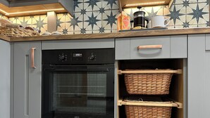 Een keuken met grijze kastjes, een zwarte oven en rieten manden op planken.