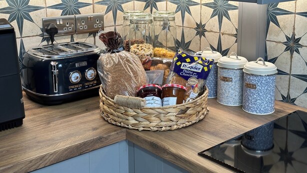 Een keukenblad met een vintage toaster, een broodmand, potten jam en een zak Pasquier chocolade.