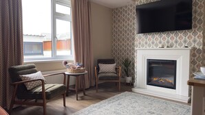 Een gezellige woonkamer met een open haard, een televisie erboven en twee fauteuils.