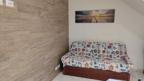 A room with a wooden floor, a sofa with a nautical-themed cover, and a sunset painting on the wall. - At Erica's house (Mascali)