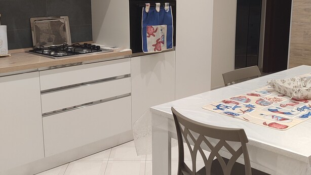 A modern kitchen with white cabinetry, a gas stove, and a dining table with a floral tablecloth. - At Erica's house (Mascali)