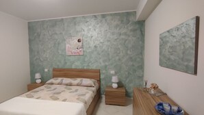 A bedroom with a bed, two bedside tables, a nightstand, a wall-mounted painting, and a wooden dresser. - At Erica's house (Mascali)