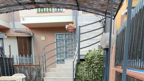 A patio area with artificial grass, a small table and chairs, a staircase, and a wall with a mural. - At Erica's house (Mascali)