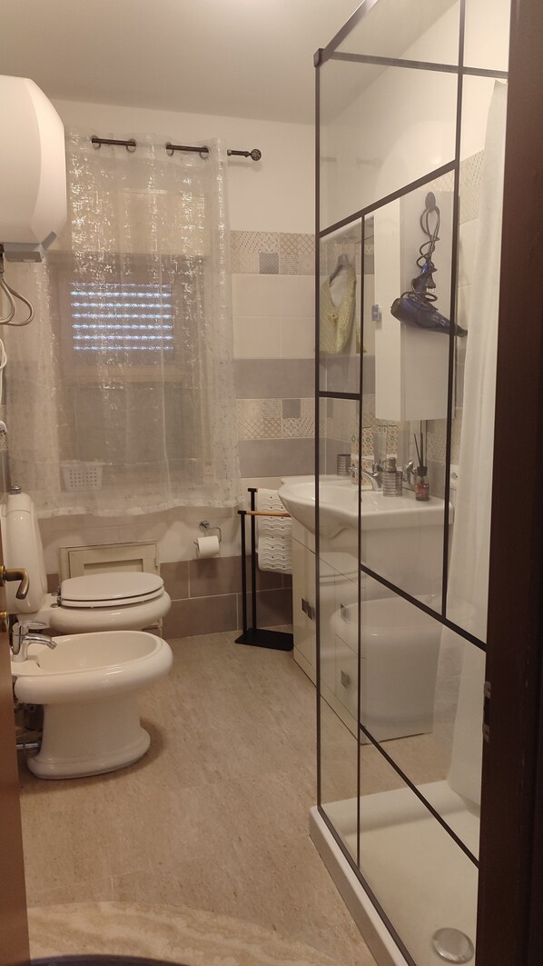 A modern bathroom with a glass shower enclosure, a toilet, a bidet, and a sink with a mirror. - At Erica's house (Mascali)