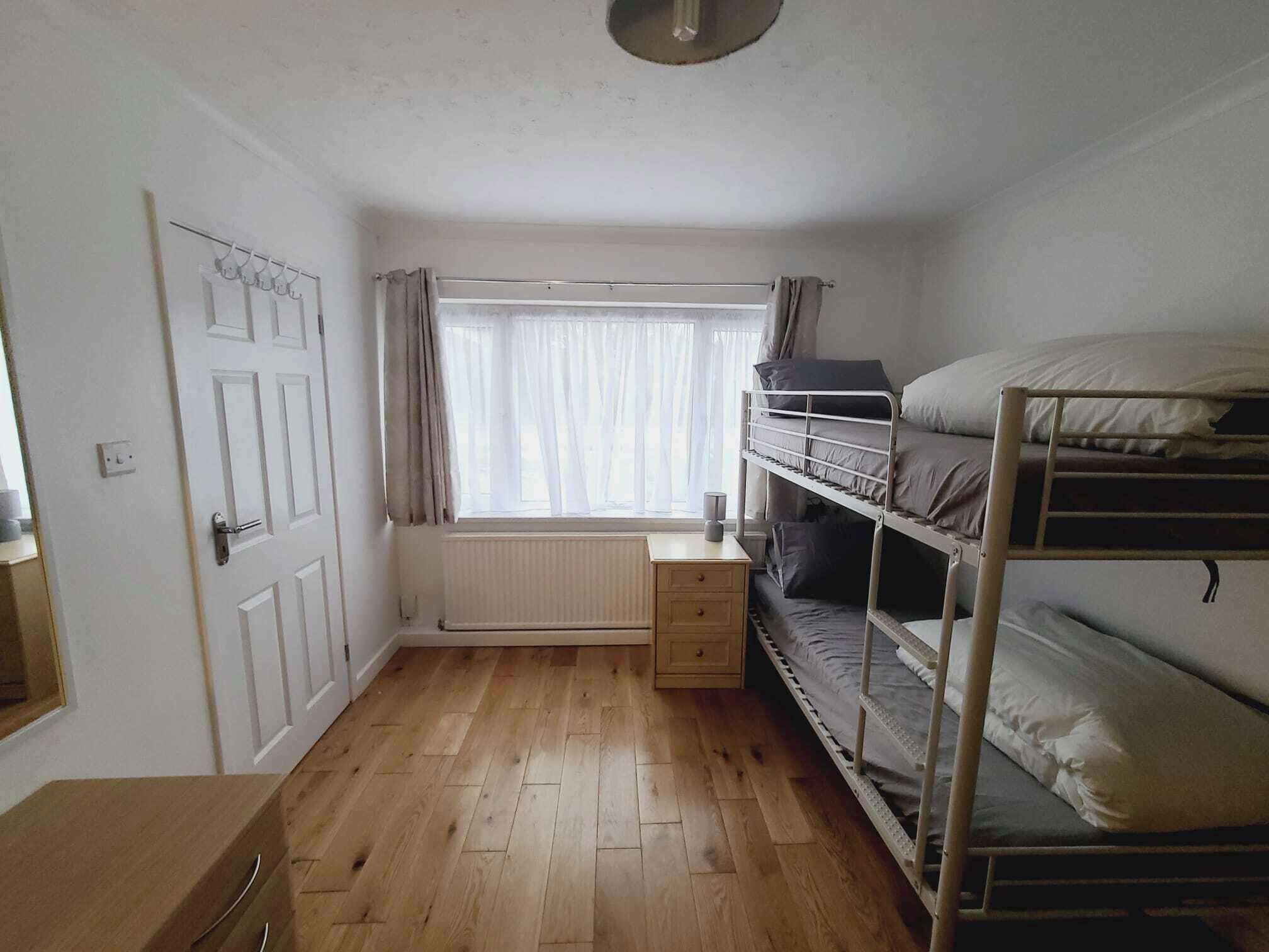 A small, single-room apartment with a wooden floor, a bunk bed, a small desk, and a radiator.