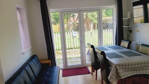 A room with a black leather sofa, a dining table with chairs, a white ceiling fan, and a view of a white picket fence and greenery outside. - Rusper Retreat - Spacious Home Near Gatwick (Crawley)