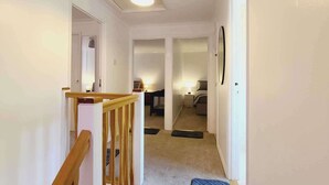 A hallway with a wooden railing, carpeted floor, and a ceiling light. - Rusper Retreat - Spacious Home Near Gatwick (Crawley)