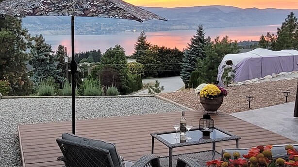 An outdoor patio with a table and chairs, a decorative umbrella, and a view of a lake and mountains. - Private Suite with Amazing Lake View (Naramata)