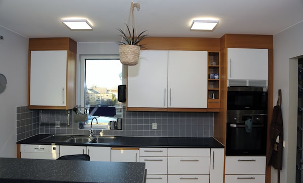 A modern kitchen with white cabinets, a black countertop, and a stainless steel refrigerator.