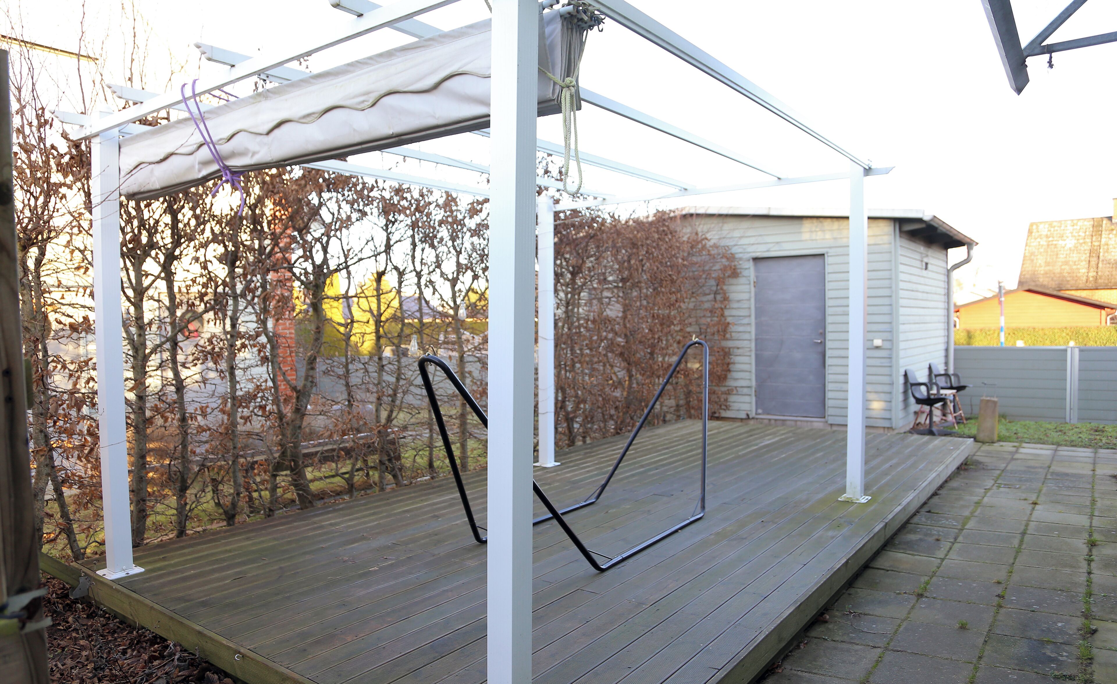 Un espacio al aire libre techado con piso de madera, vigas de metal y un toldo blanco.