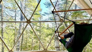 A room with a large window, a hanging chair, and a wooden floor. - The Lena Dome (Grand Marais)