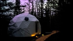 A dome-shaped tent with a door, surrounded by trees and a gravel path. - The Lena Dome (Grand Marais)
