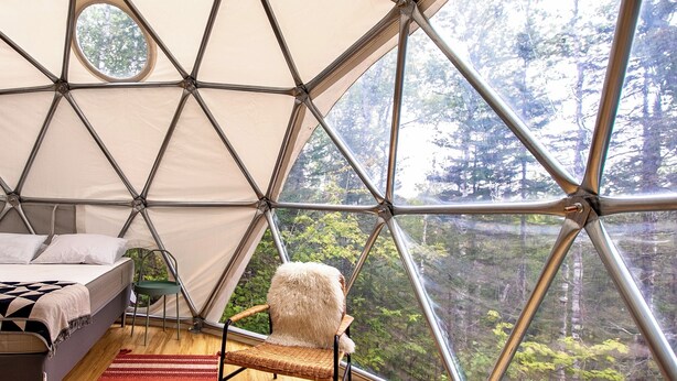A geodesic dome interior with a bed, a chair, and a view of a forest. - The Lena Dome (Grand Marais)