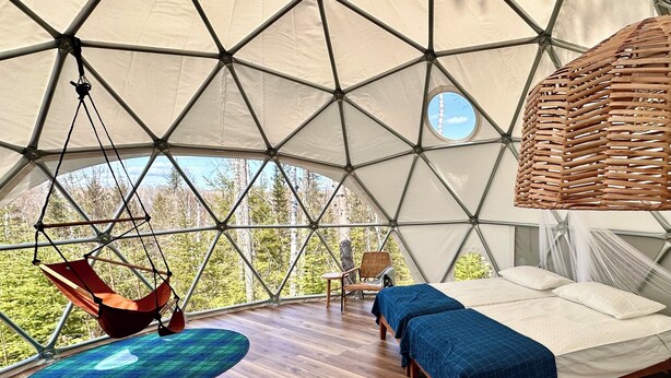 A geodesic dome tent with a bed, a hanging chair, and a small table.